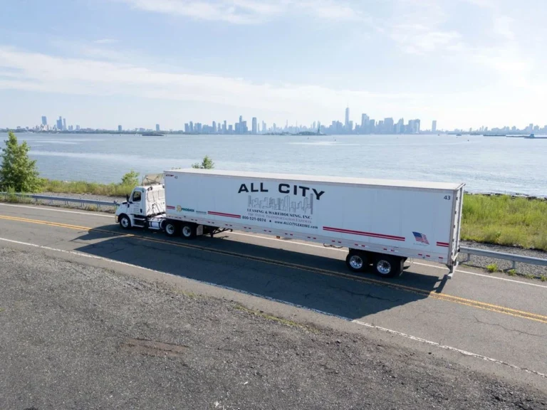 All City Leasing semi truck driving along a riverside highway with the Manhattan skyline in the background