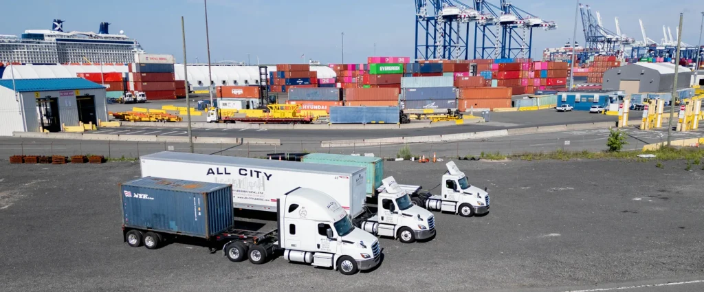 Three All City Leasing semi-trucks parked near colorful shipping containers and port cranes at a busy international freight terminal